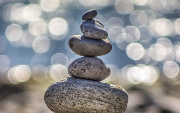 Balance Steinmännchen aus fünf Steinen, im Hintergrund verschwommenes Wasser und Lichtreflexe.