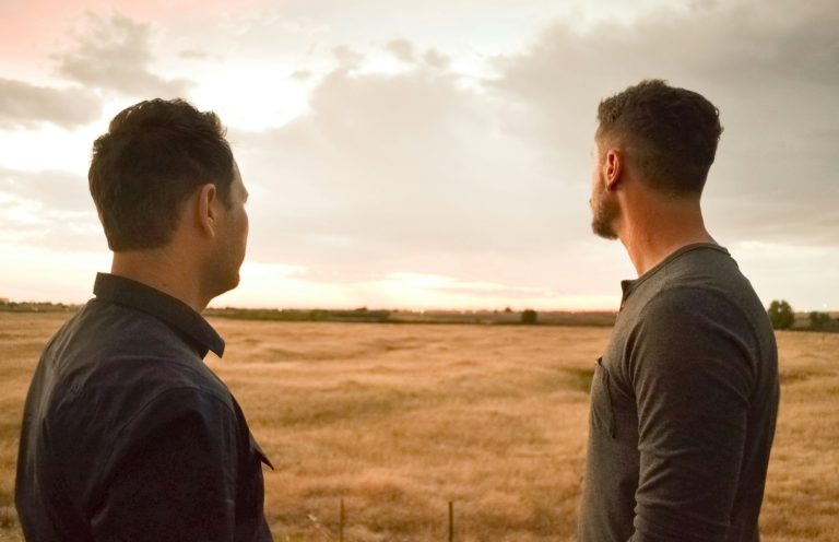 Umgang mit schwierigen Themen Zwei Männer stehen auf einem Feld und schauen auf einen Sonnenuntergang.